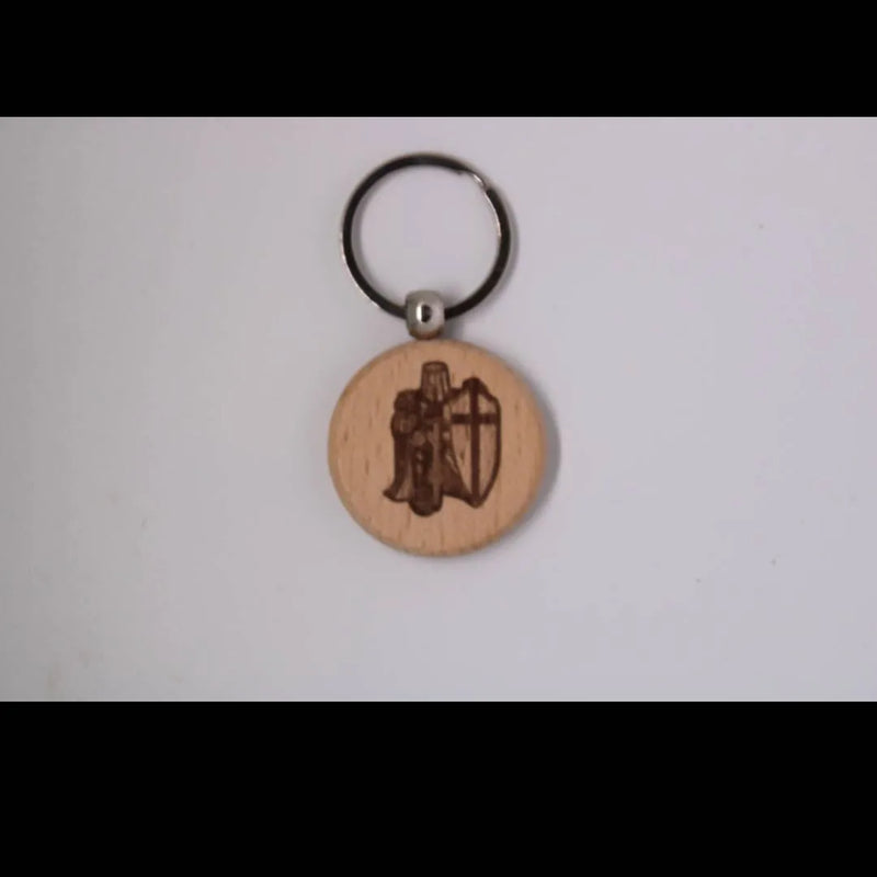 A round wooden keychain charm engraved with a knight and shield design, attached to a black metal key ring, shown against a plain light background.