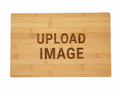 A rectangular bamboo cutting board with a natural light wood grain texture, featuring the words 'UPLOAD IMAGE' engraved in the center, set against a plain white background.